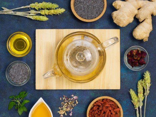 Top-view moringa infusion tea in a glass teapot, surrounded by fresh moringa leaves and ginger.